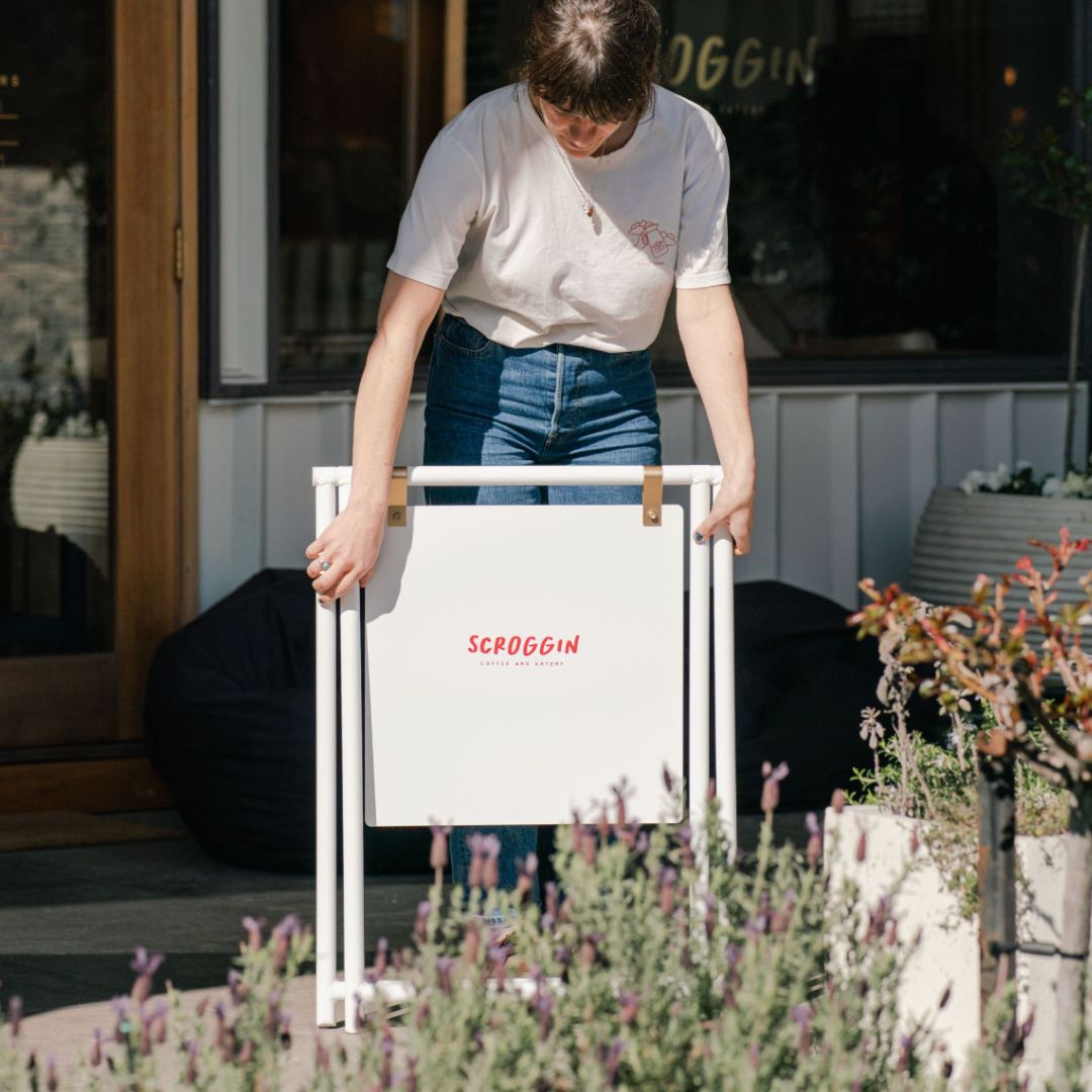 Barista carrying portable white A Frame pavement sidewalk sign with restaurant branding on front panel