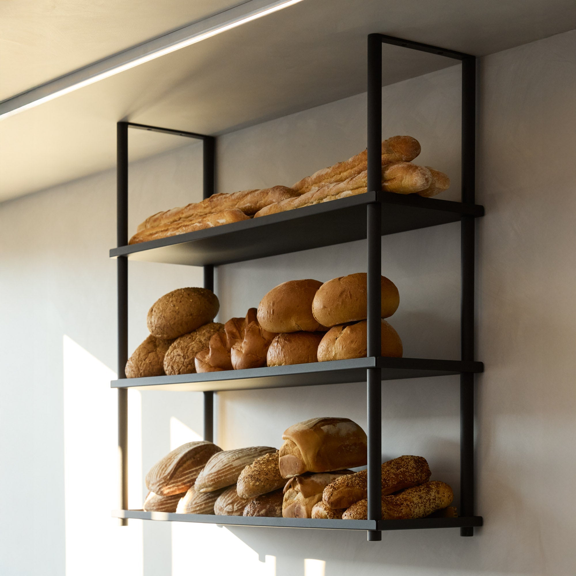 angled photo of black ceiling mounted shelves displaying bread at a bakery