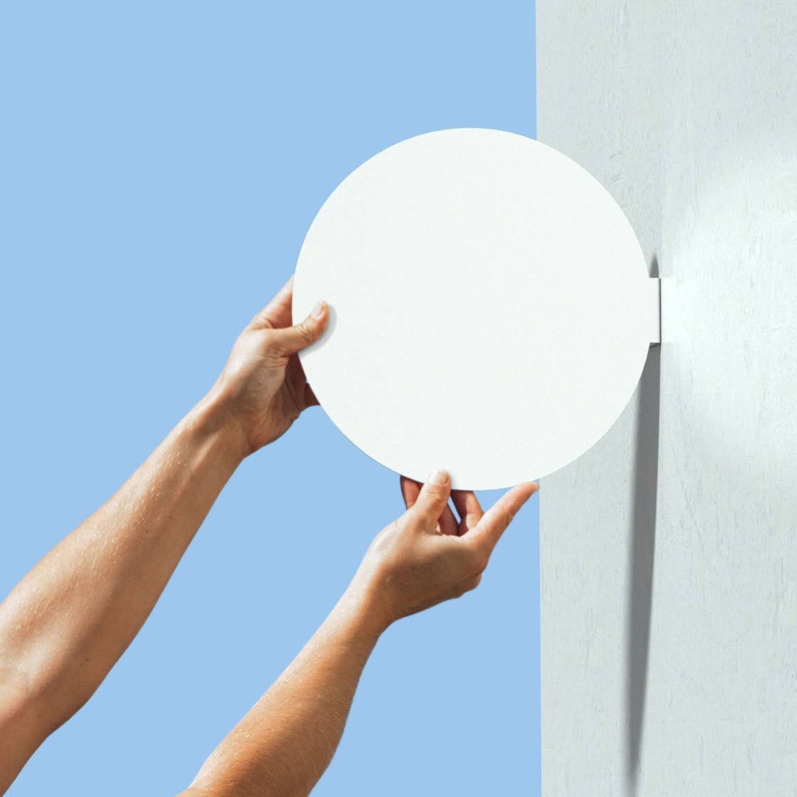 two hands holding up a plain white circle blade sign to show wall mount