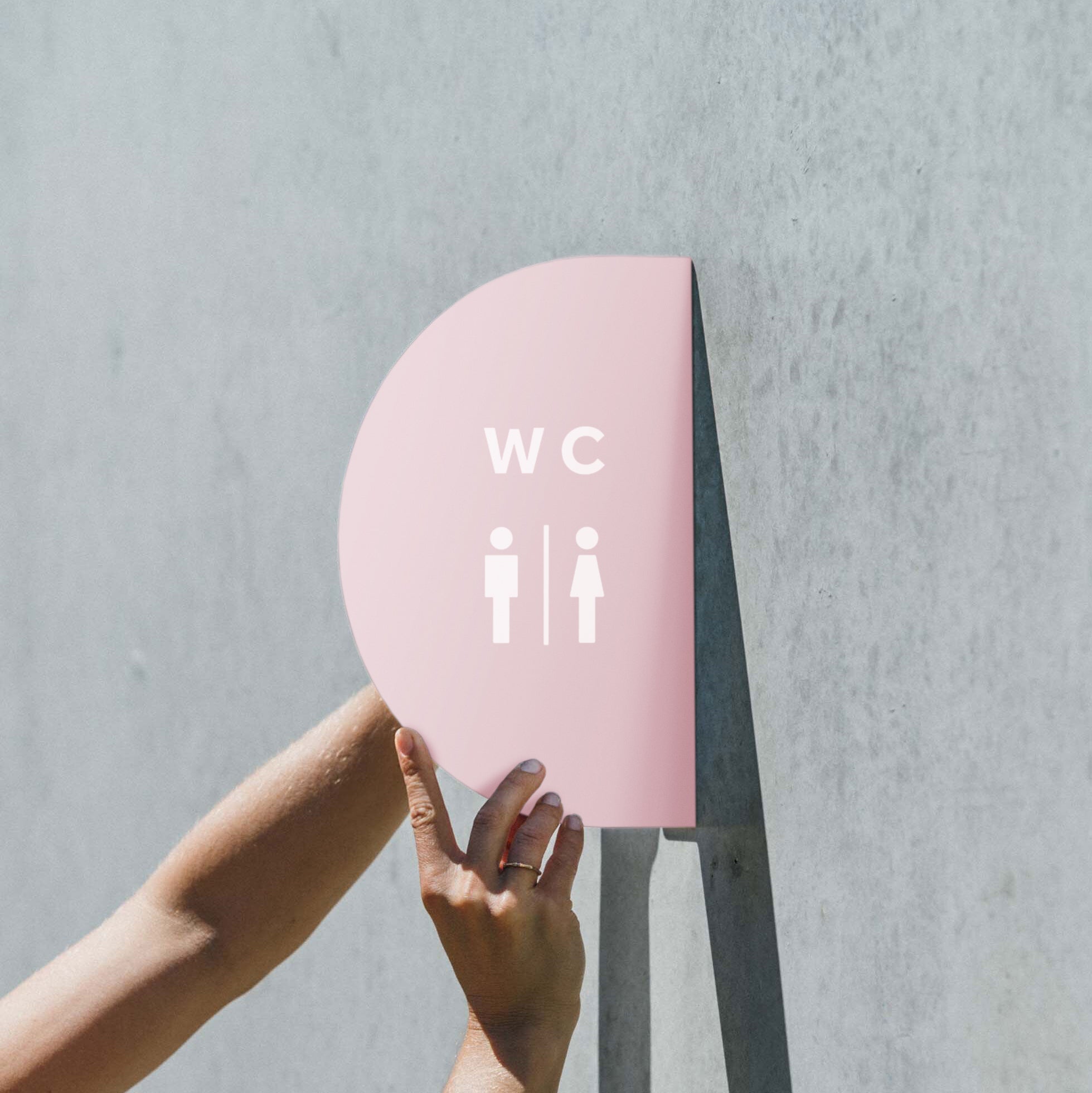 two hands holding/installing the pink half round blade sign with toilet sign decals