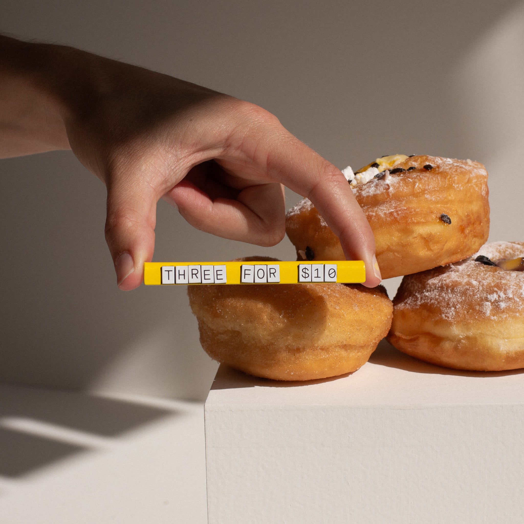 hand picking up large yellow pricing sign in front of pastries