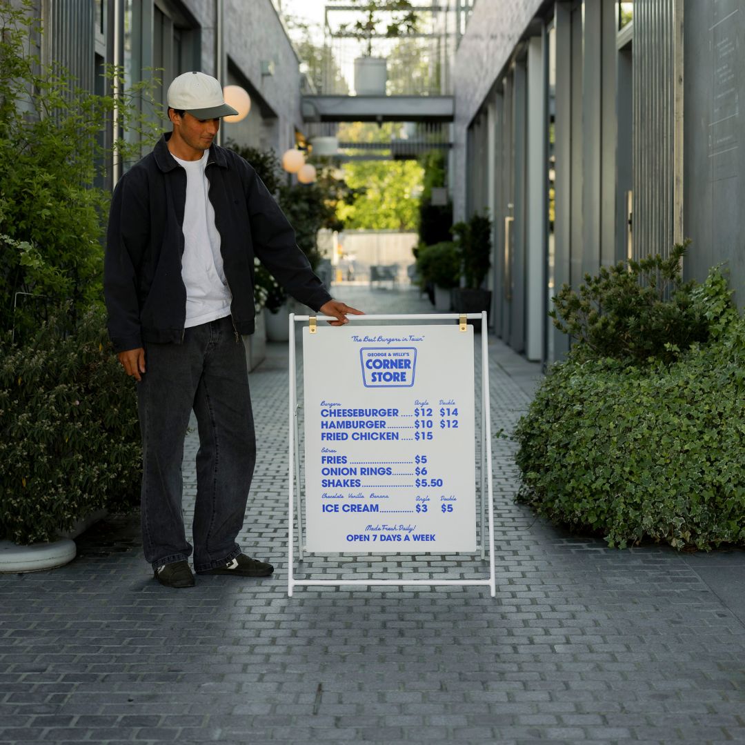 white large sidewalk sign in an alleyway with a person standing beside it