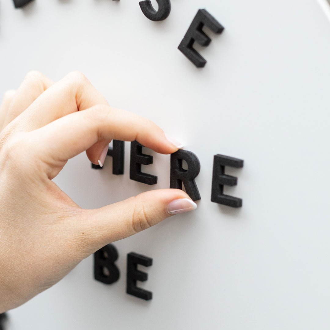 hand applying black magnet letters to white surface