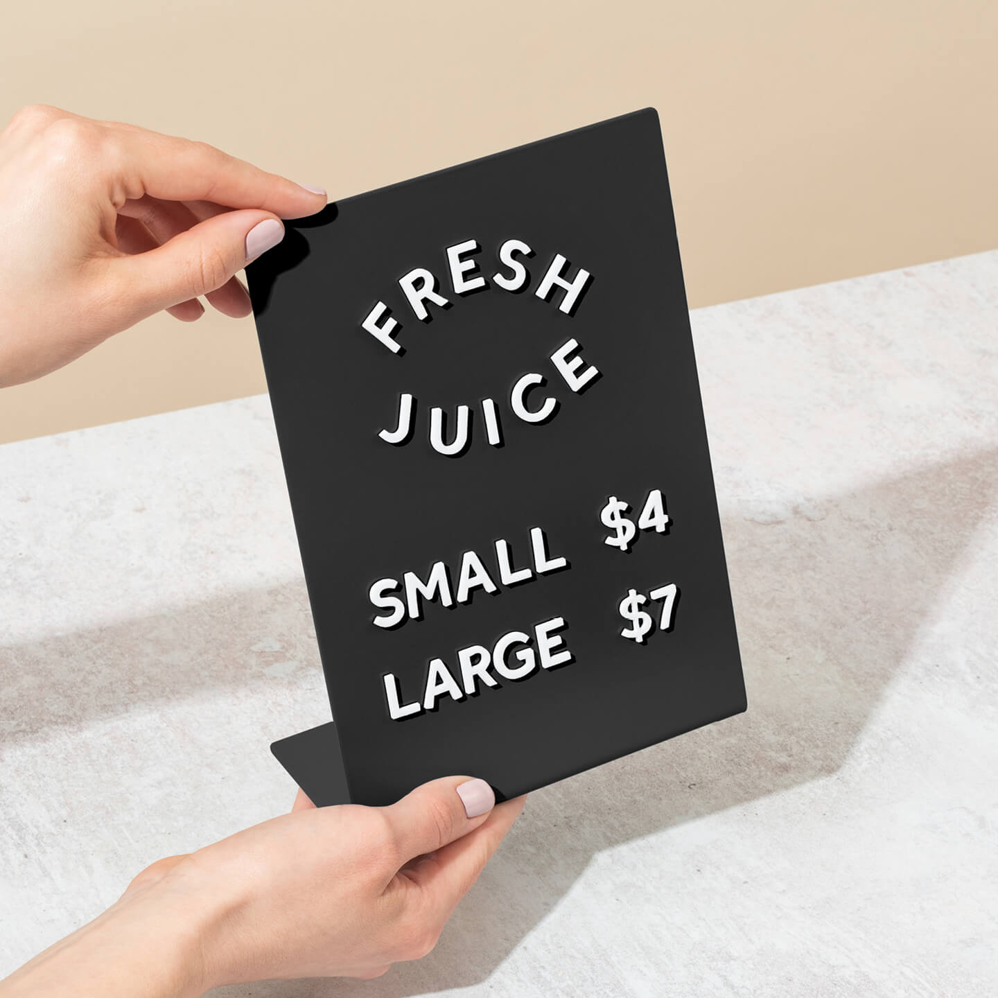 two hands holding a counter sign with magnet letters used to display juice prices