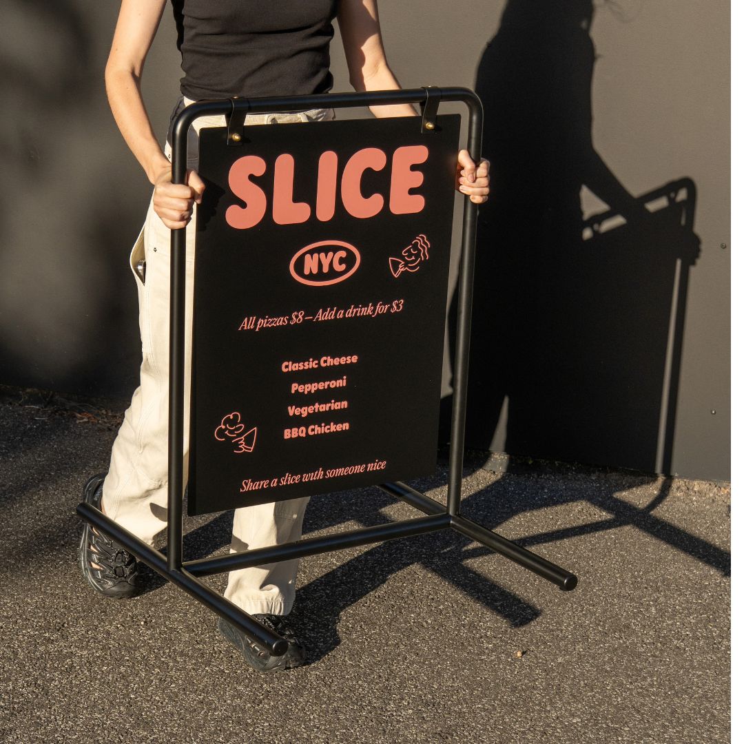 person carrying the black metal swing sandwich board sign across sidewalk