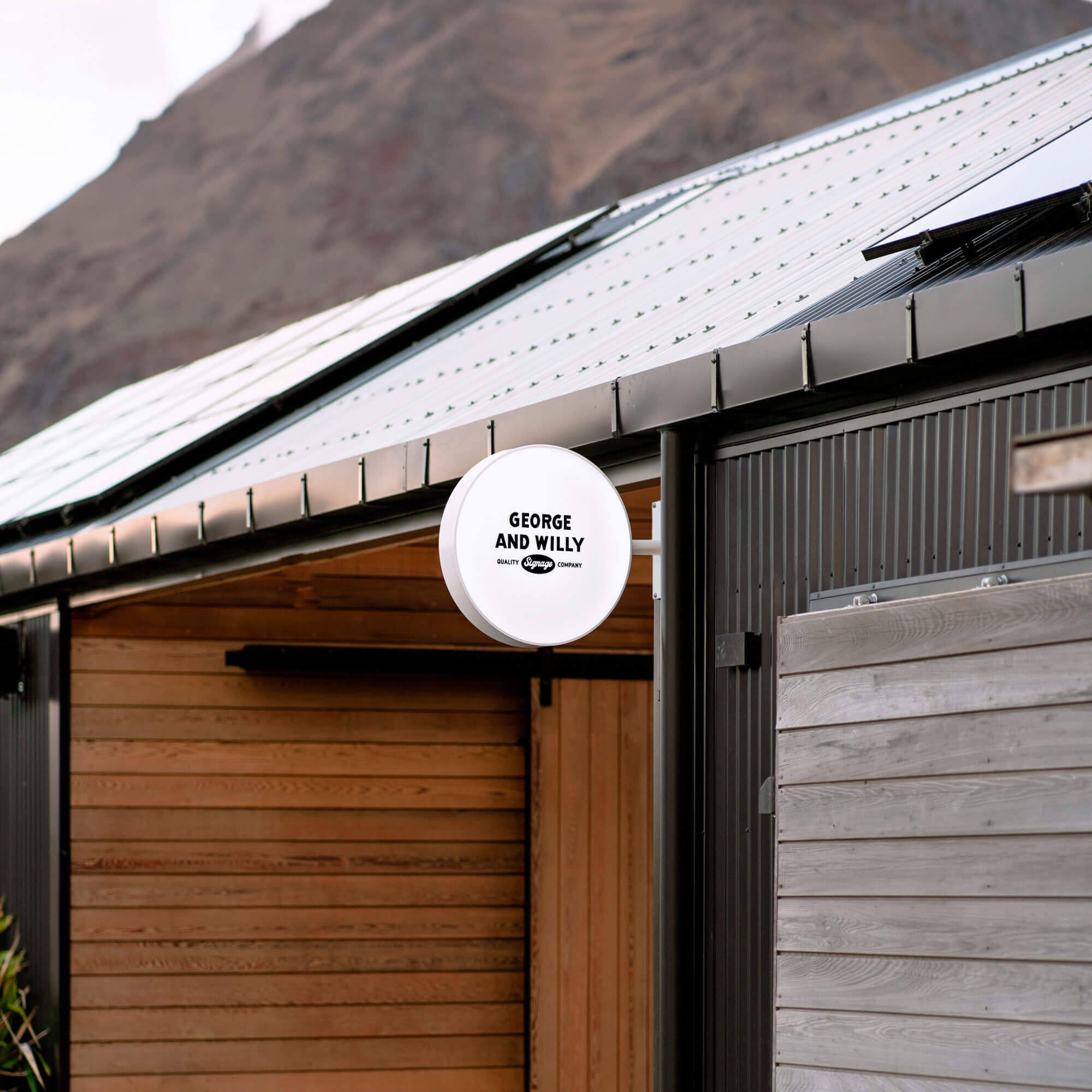 round light box wall sign installed outside a shed on a wooden beam, lit up in the day