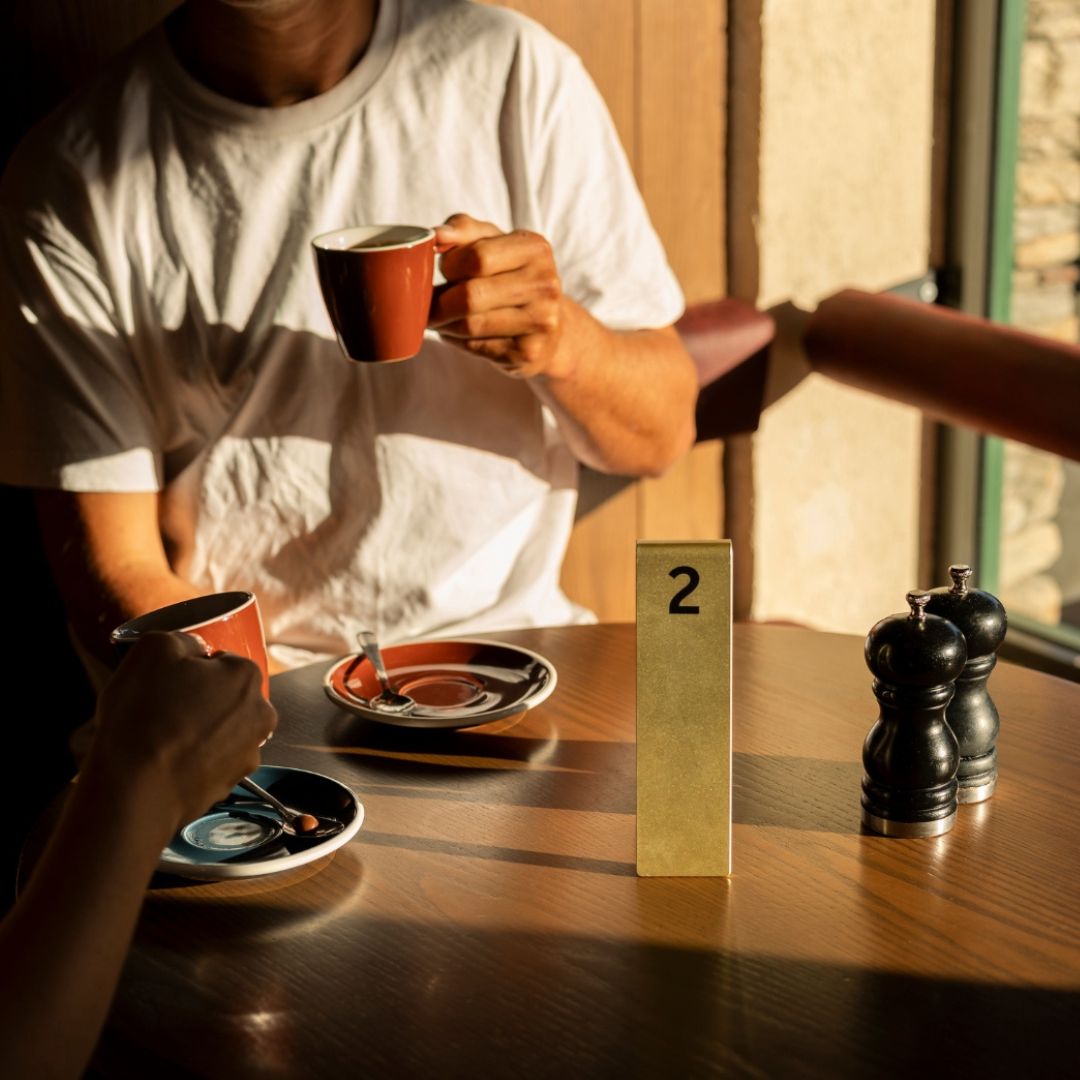 Aluminum table tent in brass finish on wooden table in cafe interior with person drinking coffee