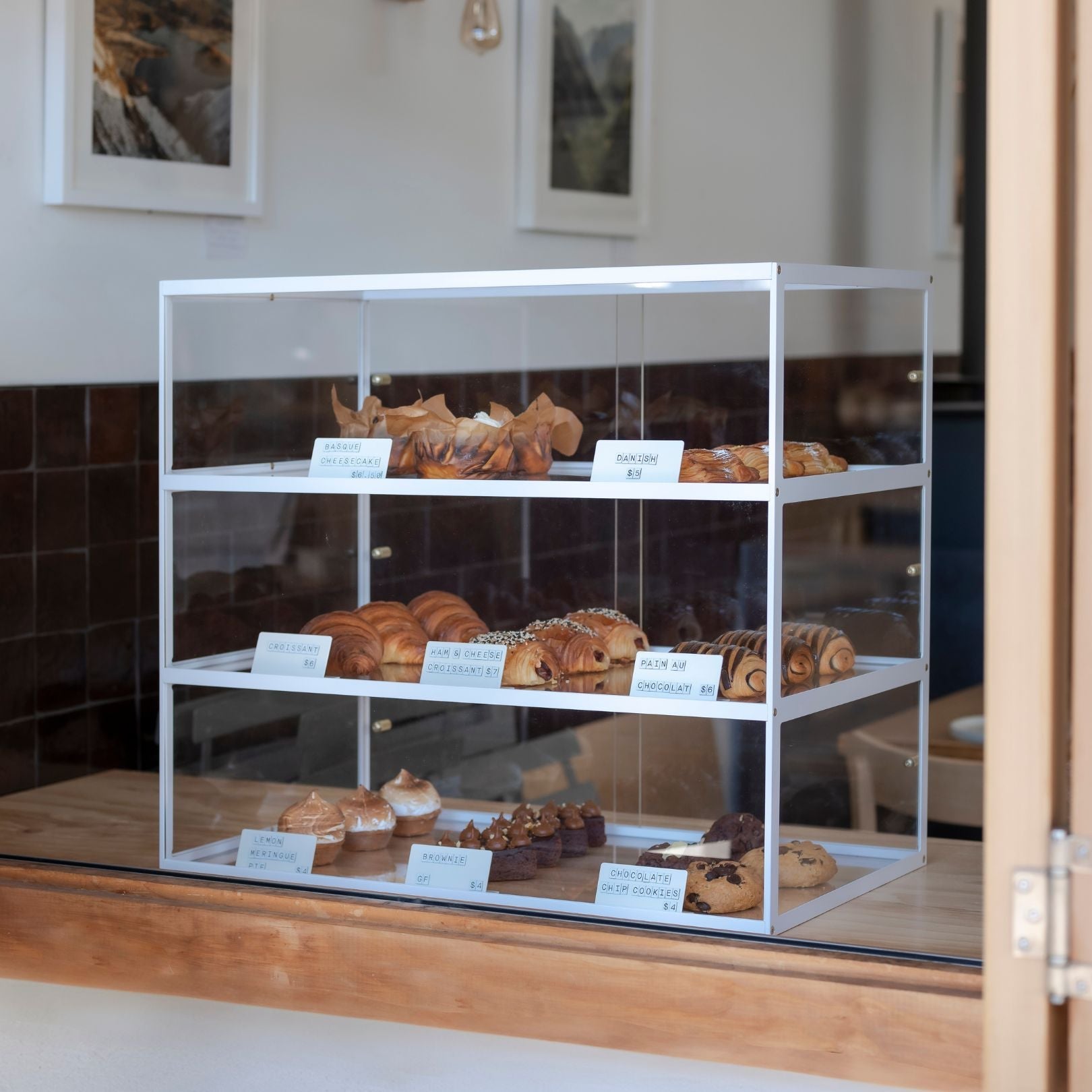 white three tier bakery acrylic display case with baked goods sitting at a cafe window