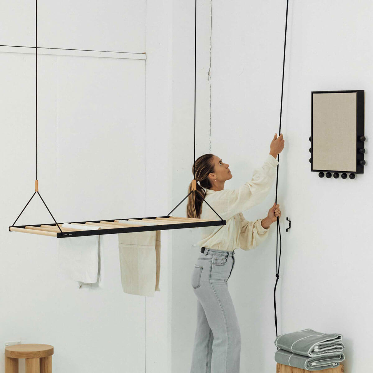 person pulling rop on ceiling hanging drying rack in a white room