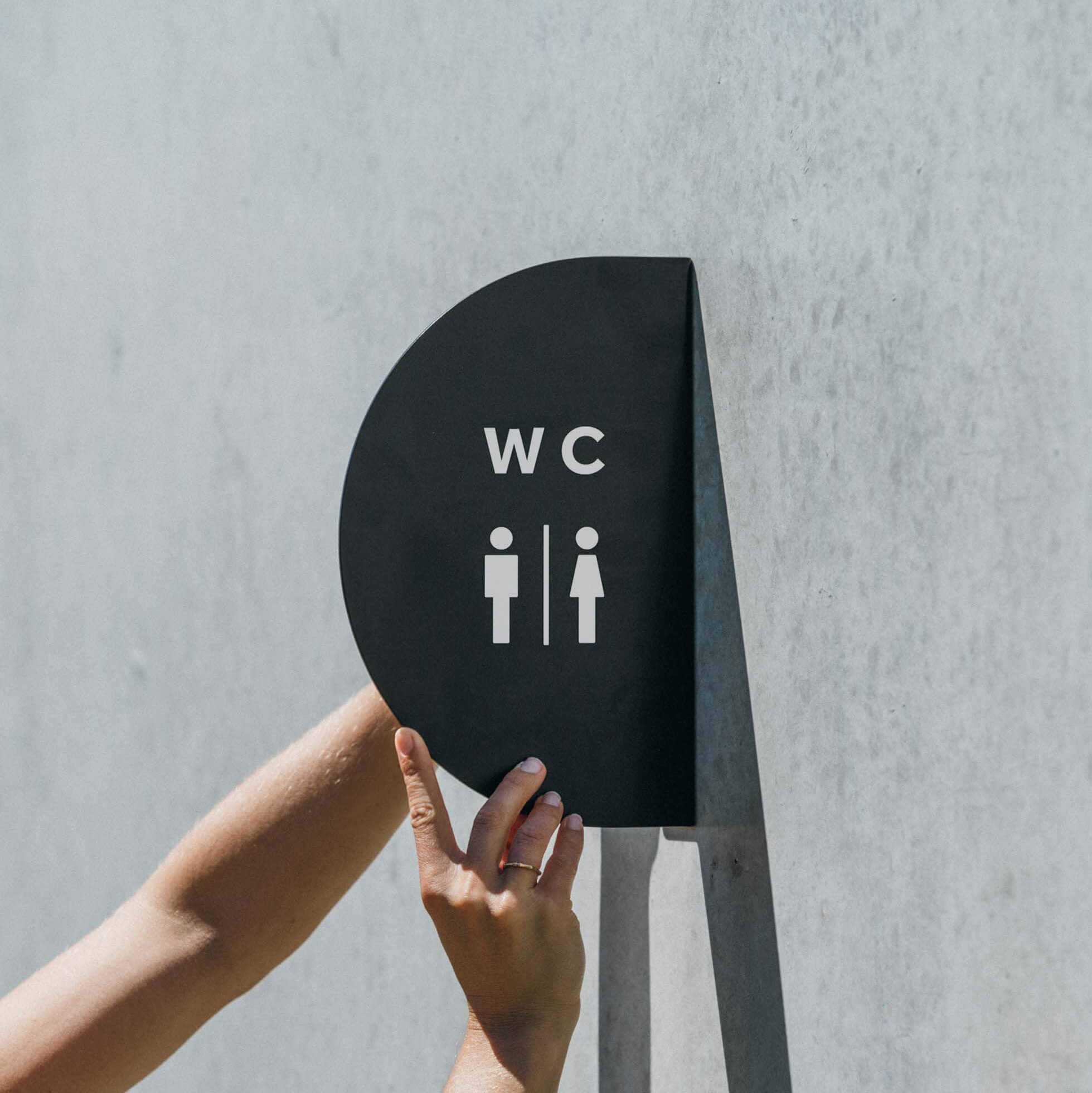 two hands holding/installing the black half round blade sign with toilet sign decals