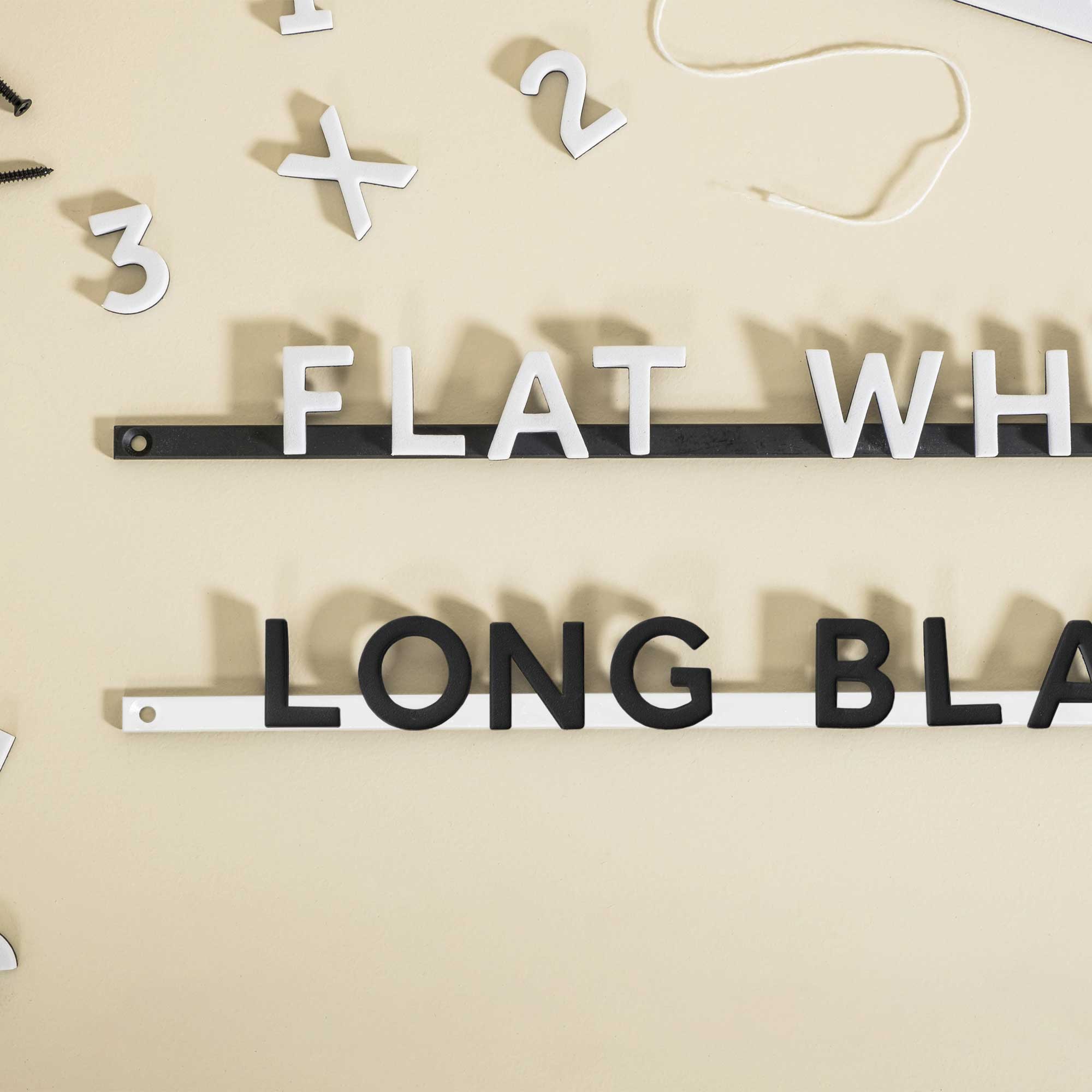white and black magnet letters on the reverse coloured rails, spelling out the start of "flat white" and "long black"