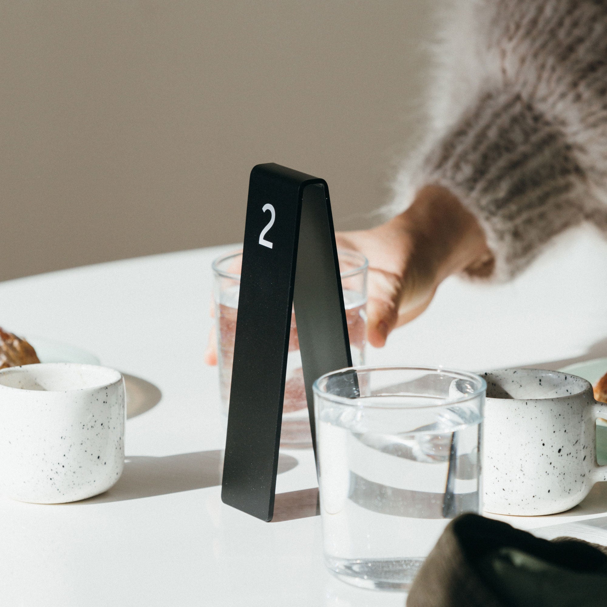 Black aluminum table number tent with laser etched number, waitress preparing drinks behind