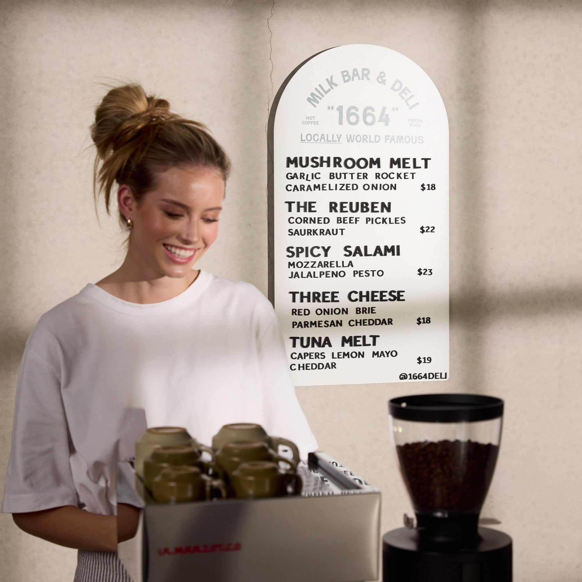 white arch menu display with deli menu displayed behind a girl making coffee on coffee machine