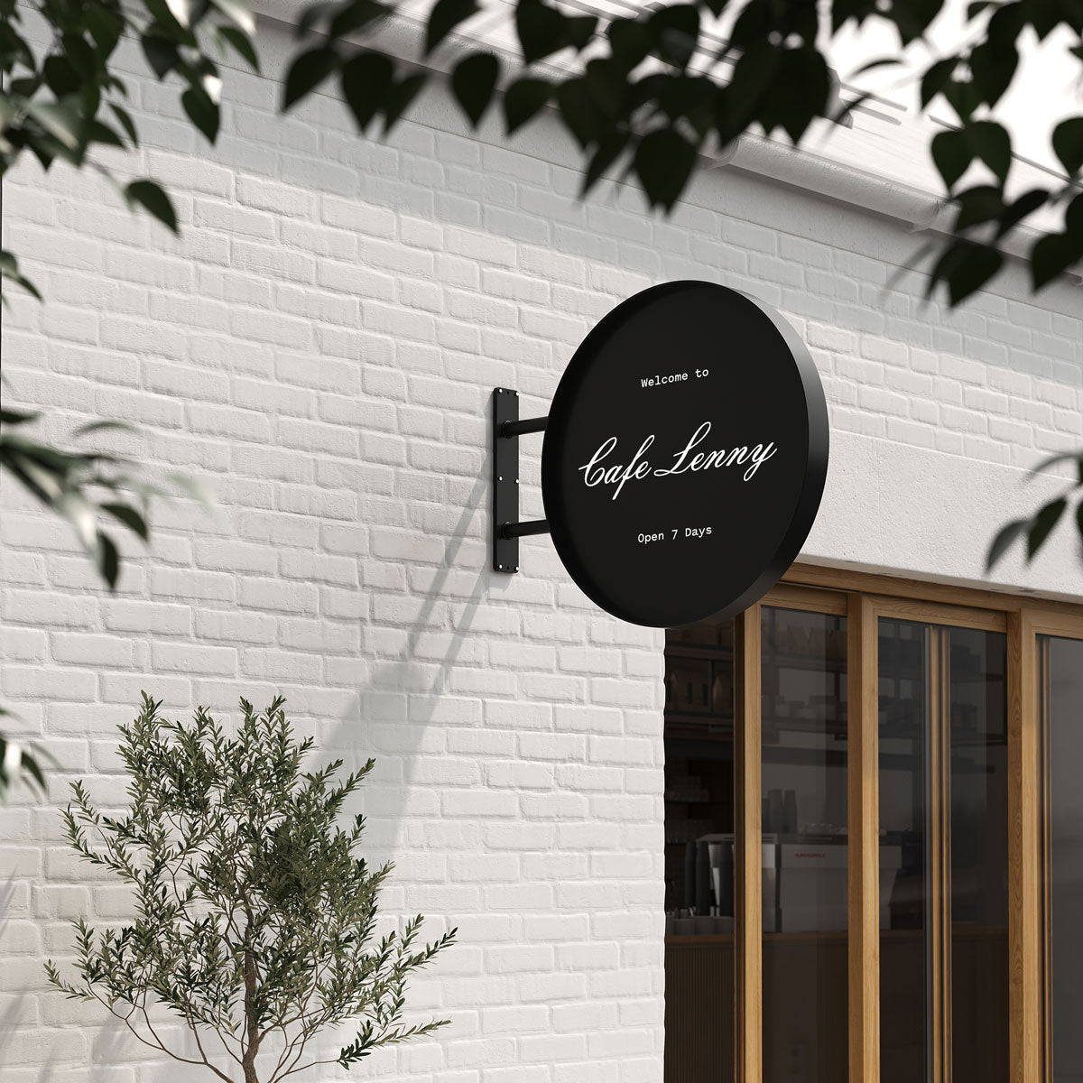 Big round sign in black finish with café logo, fixed on white brick wall with greenery