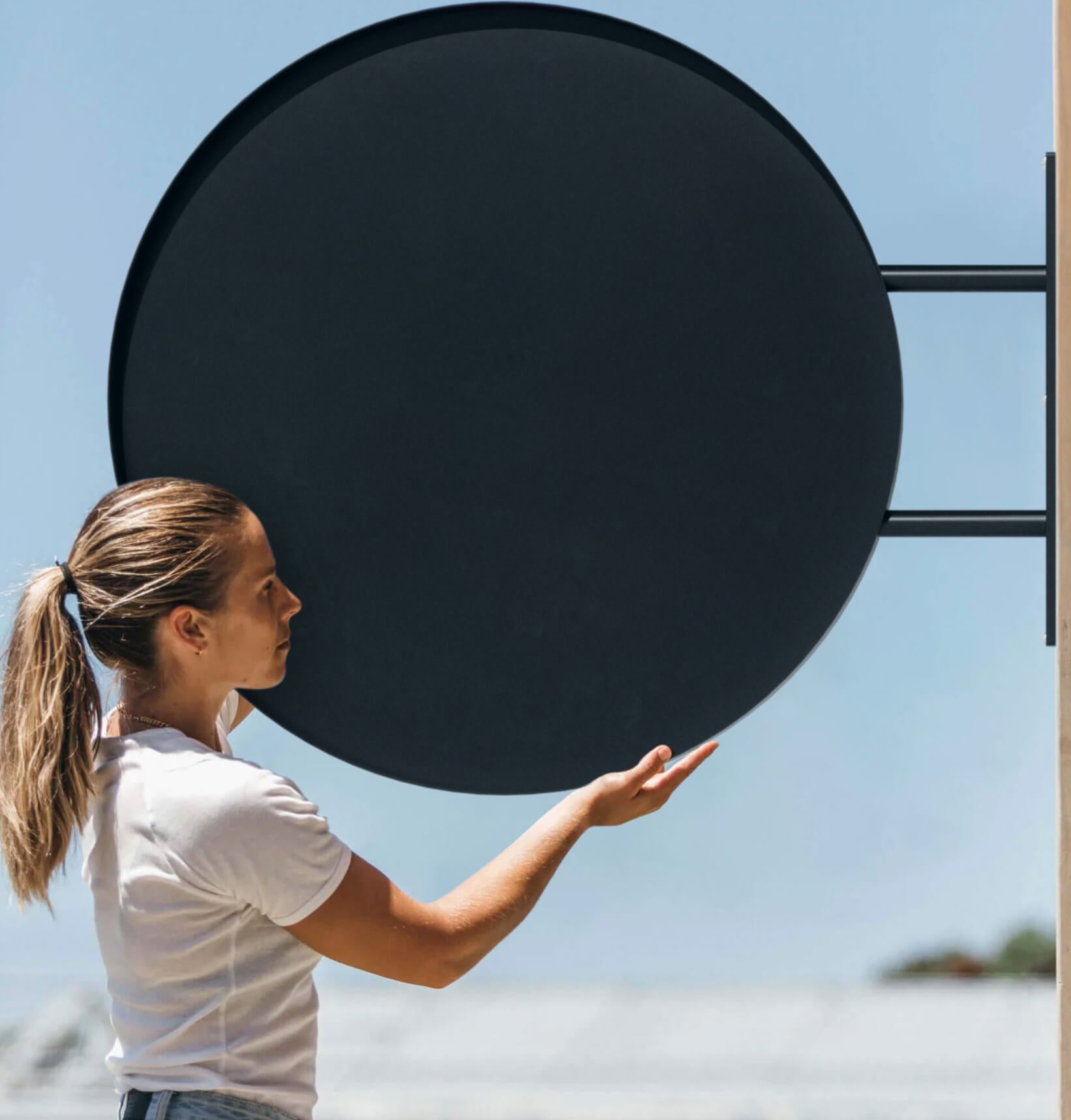 Person holding large round sign in black finish, showing scale and dimensions, preparing for wall installation