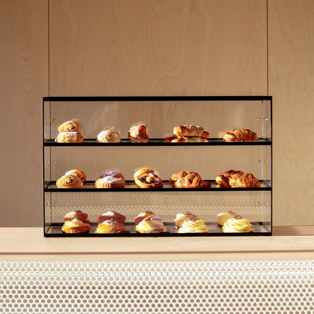 black three-tier pastry acrylic display case  with pastries inside sitting on countertop 