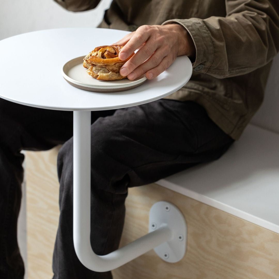 wall mounted cafe table in a restaurant setting holding a plate of pastries with person sitting beside it