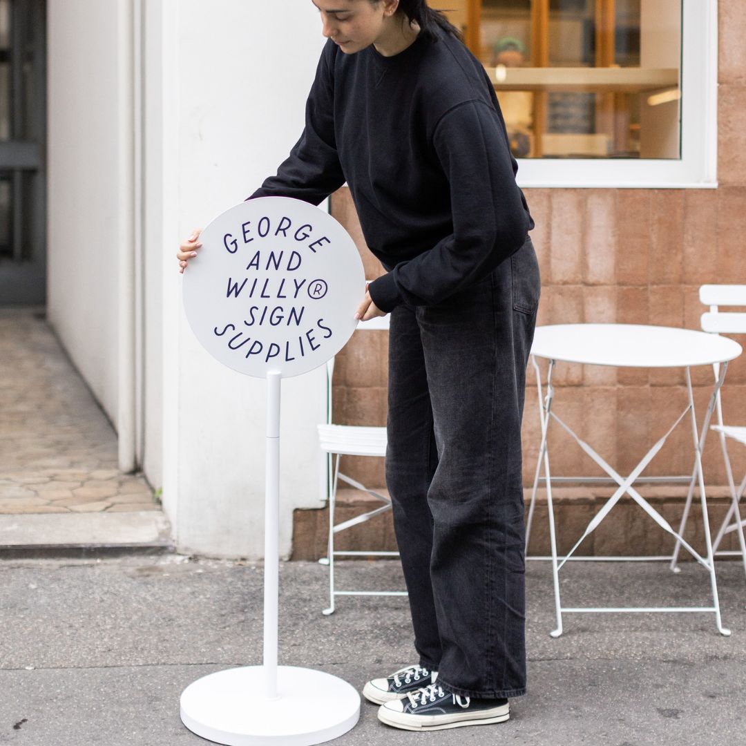 metal standing round sign with logo being placed on sidewalk by person