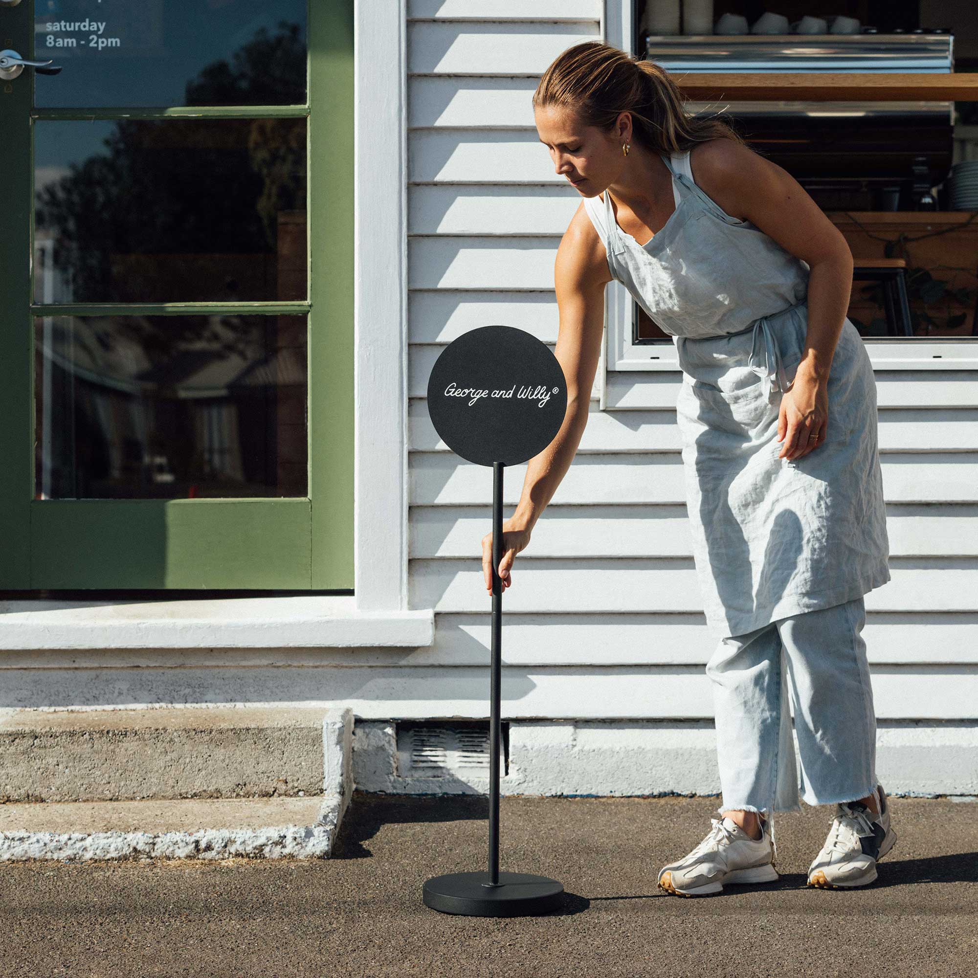 black metal freestanding round sign with logo being placed on sidewalk by person