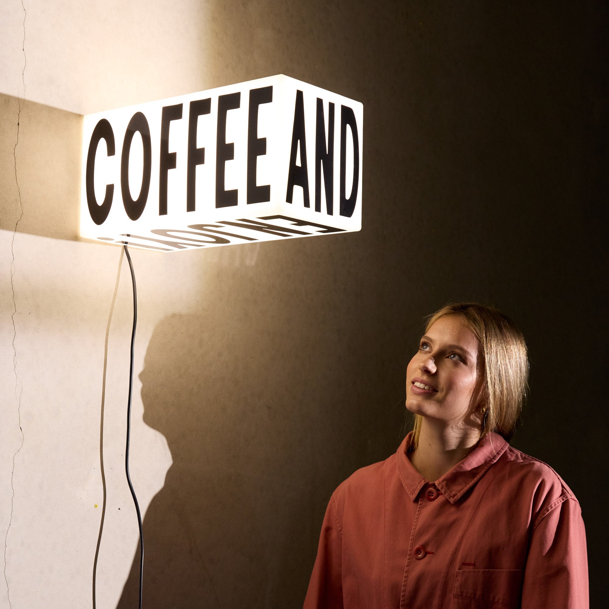 3D plastic lit up sign in warm white, mounted behind a barista prepping coffee