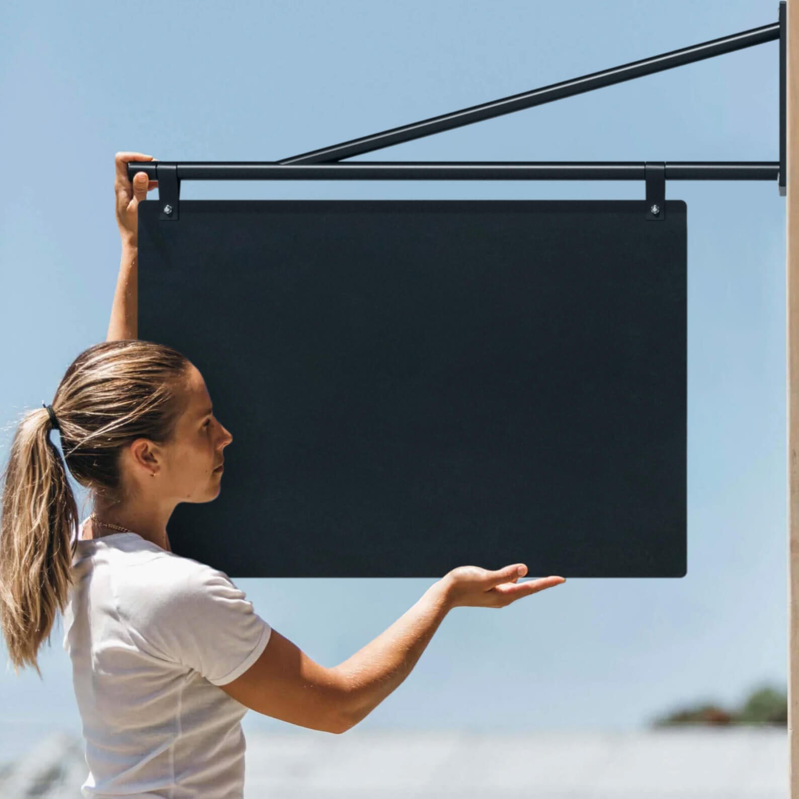 girl putting up the large black hanging store sign on the brackets