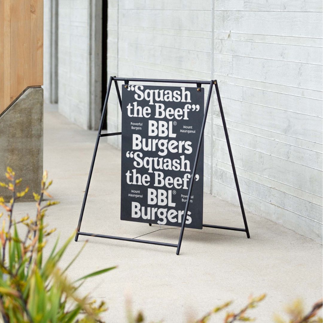 black large sidewalk pavement sign outside on a pavement against a concrete building