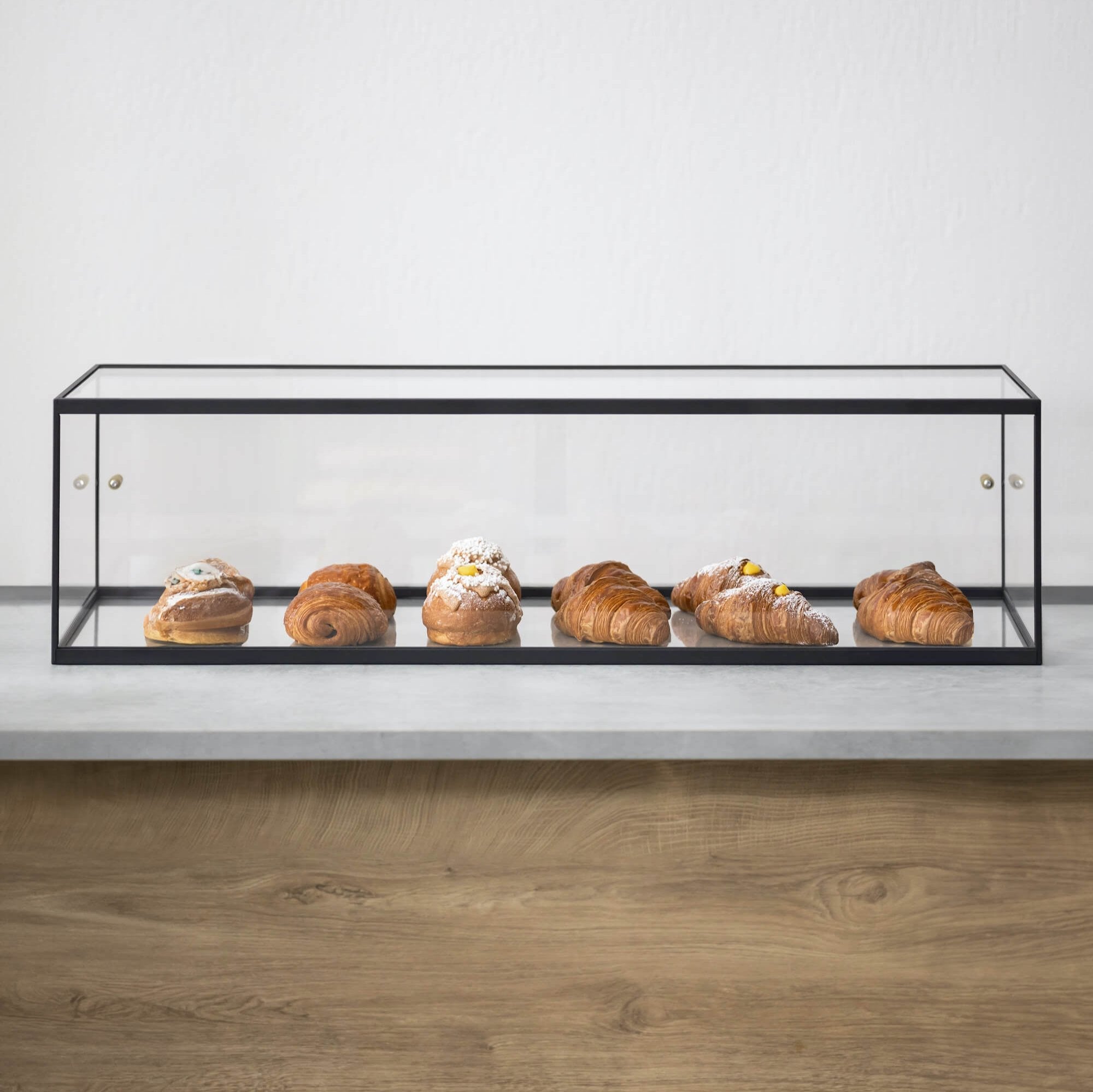 Long, acrylic pastry display case with one shelf of croissants against white background