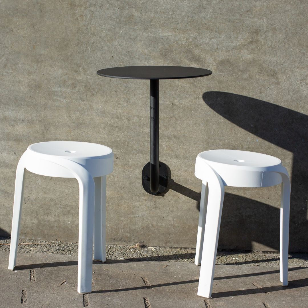 Black wall mounted cafe table mounted ouside restaurant patio on concrete wall with two small white stools