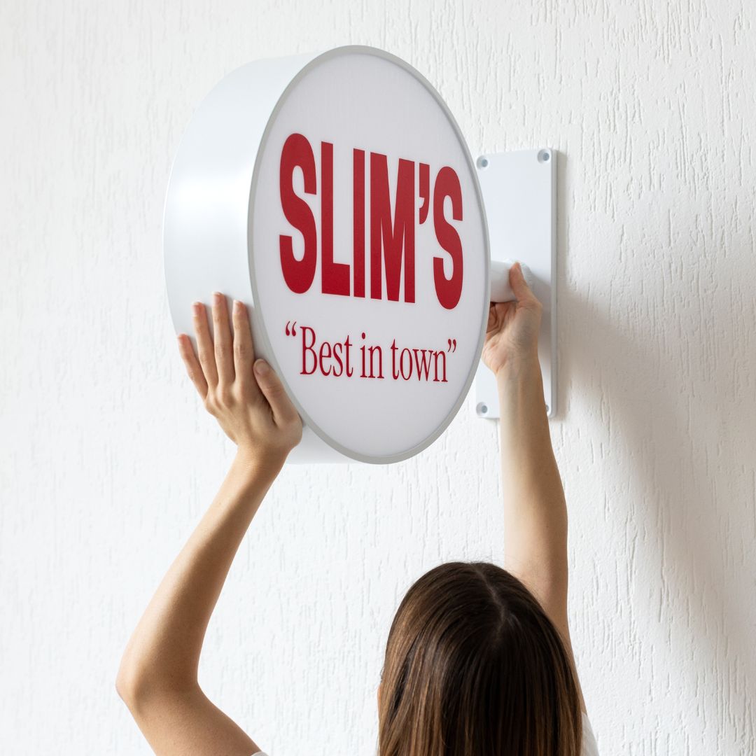 person holding and installing round light box sign on a wall