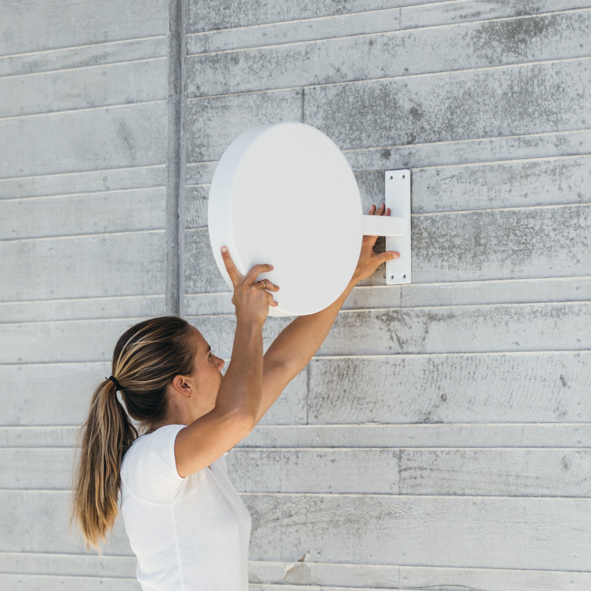 plain white round sign being mounted on a wooden wall by a girl