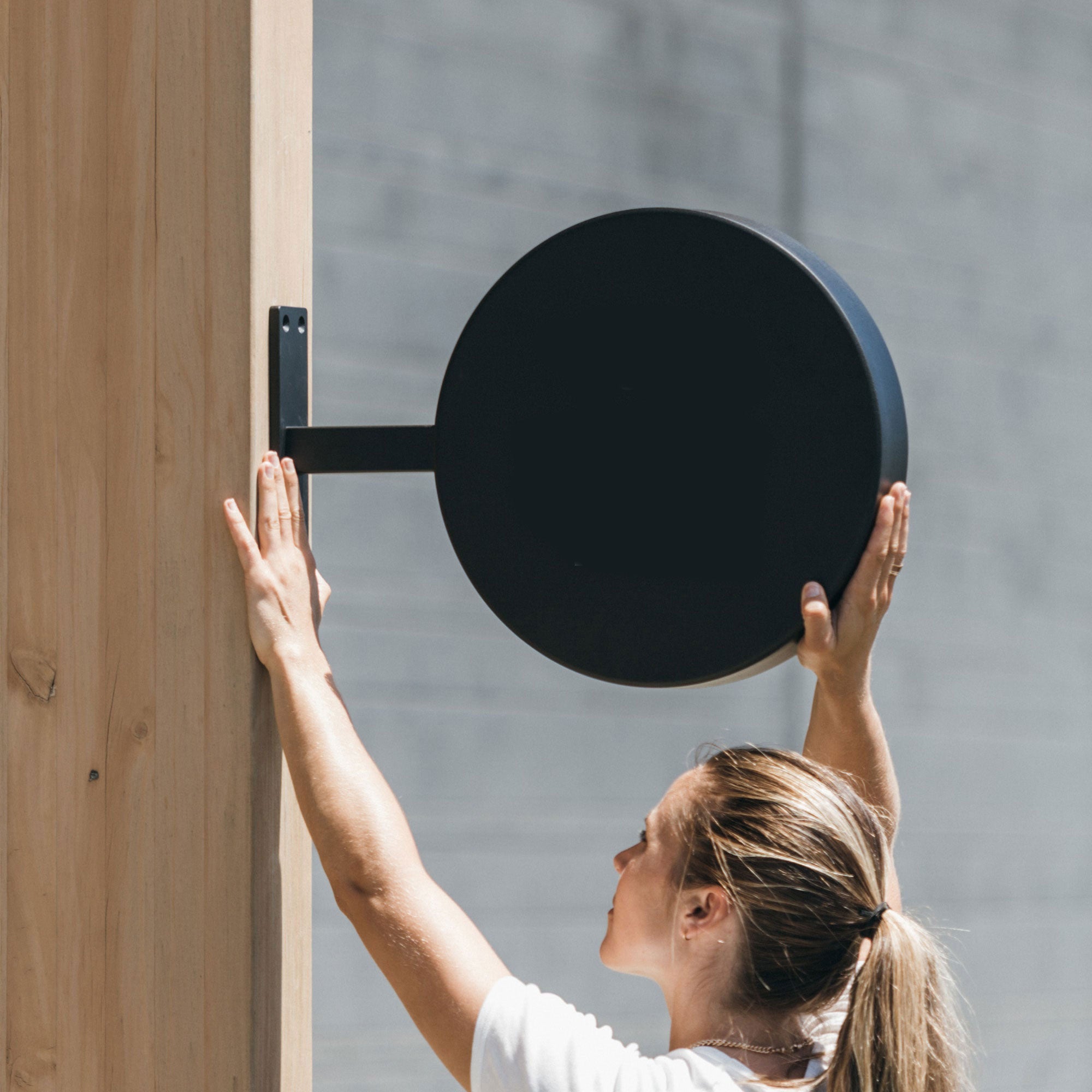 plain black round sign being mounted by a girl on a wooden beam