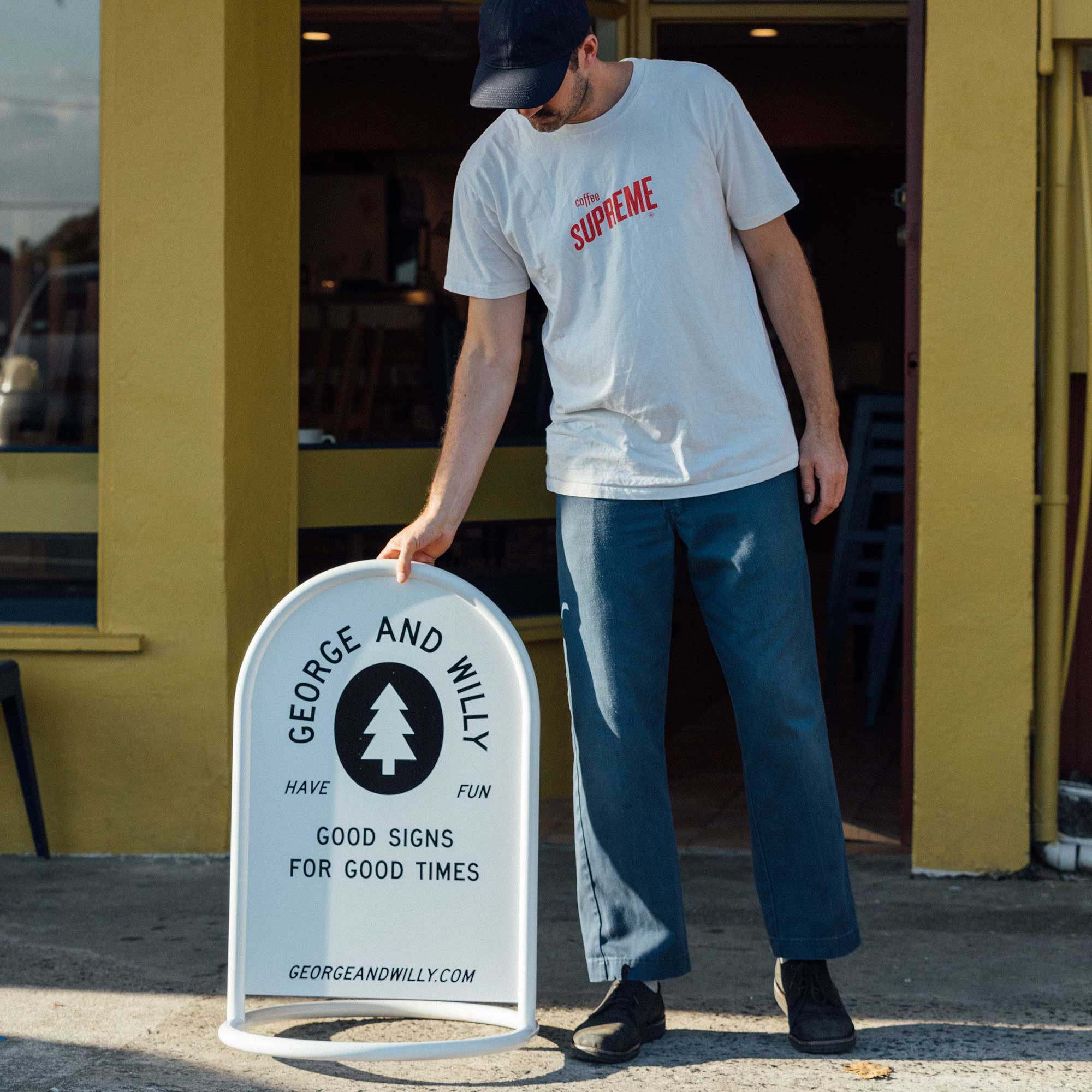 person putting white rounded custom metal signage out on sidewalk in front of yellow facade
