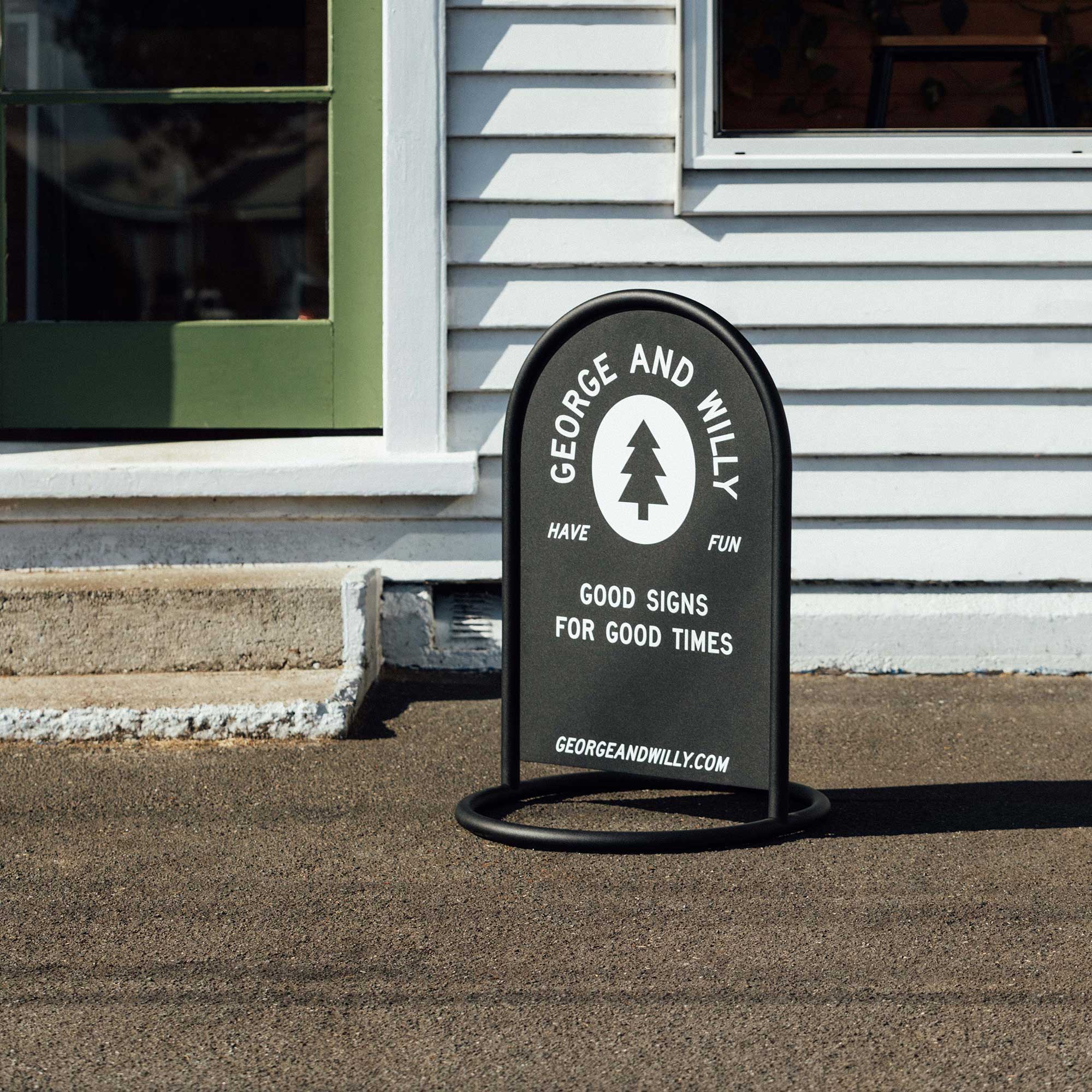 black rounded sidewalk sandwich board sign on sidewalk outside wooden business storefront