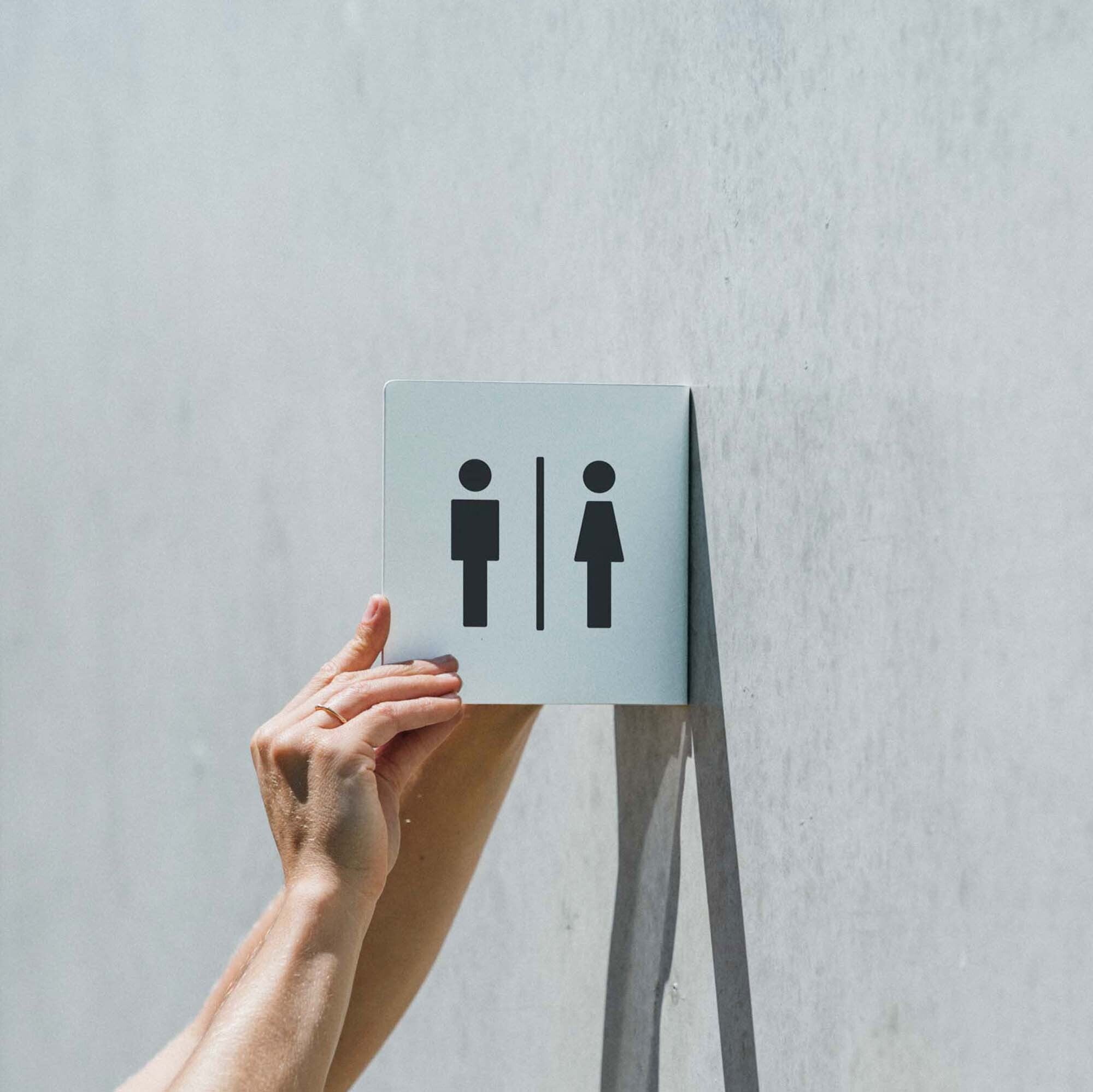 two hands installing the smaller sized square custom metal sign with bathroom decals on it