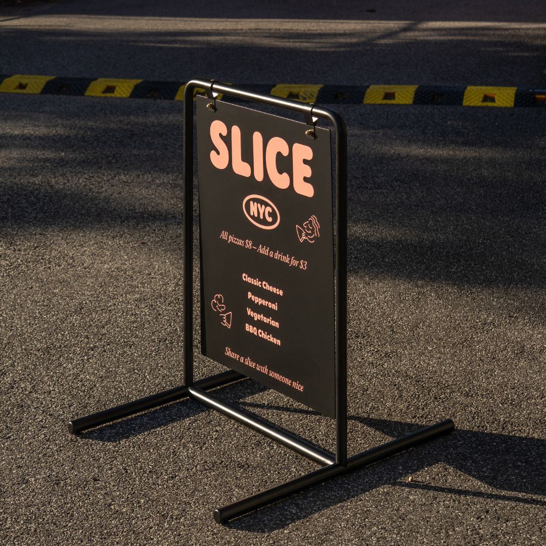 side angle profile of black metal swing business sign with golden hour light on the branding decal