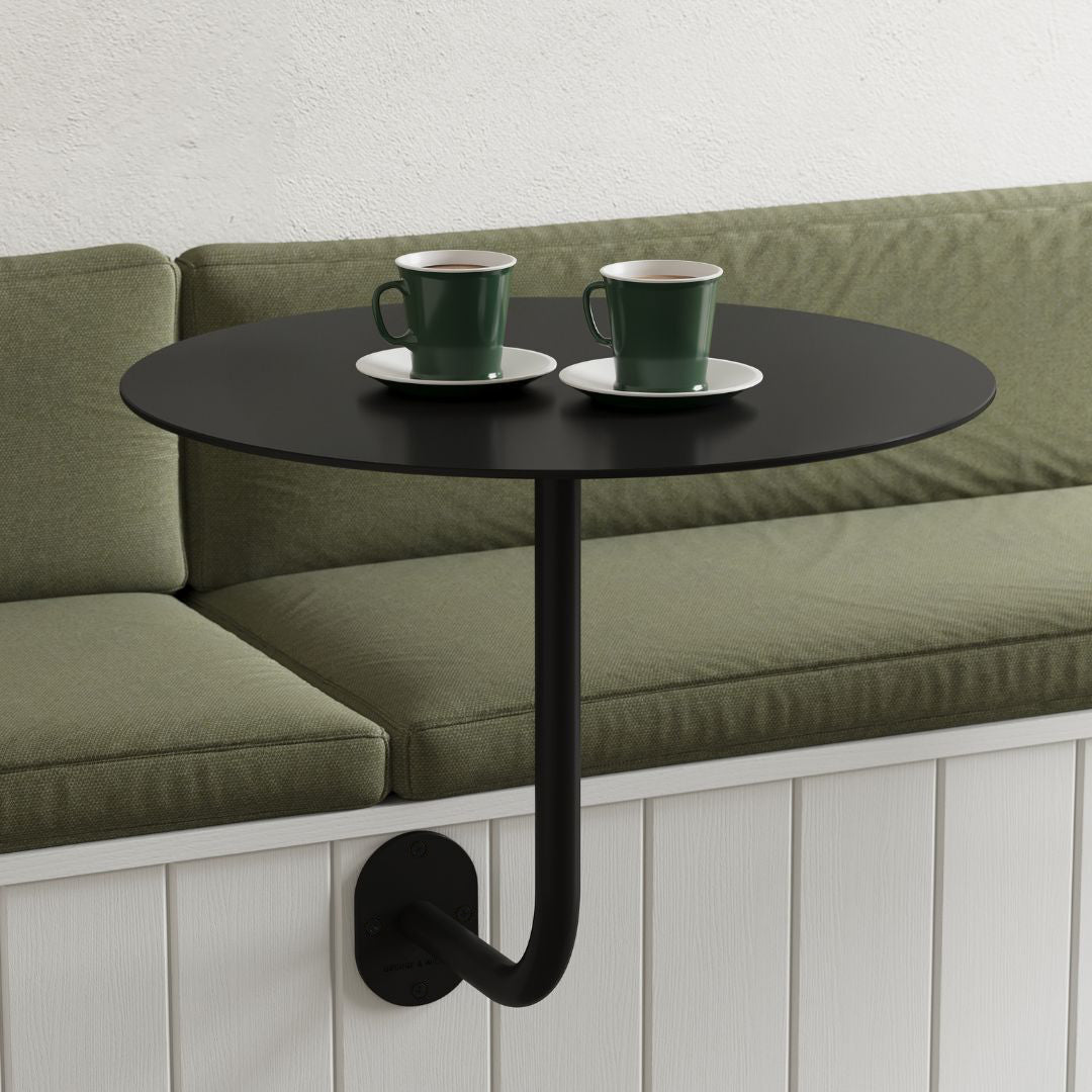 wall-mounted restaurant table in black with round cafe table top, attached to booth seat