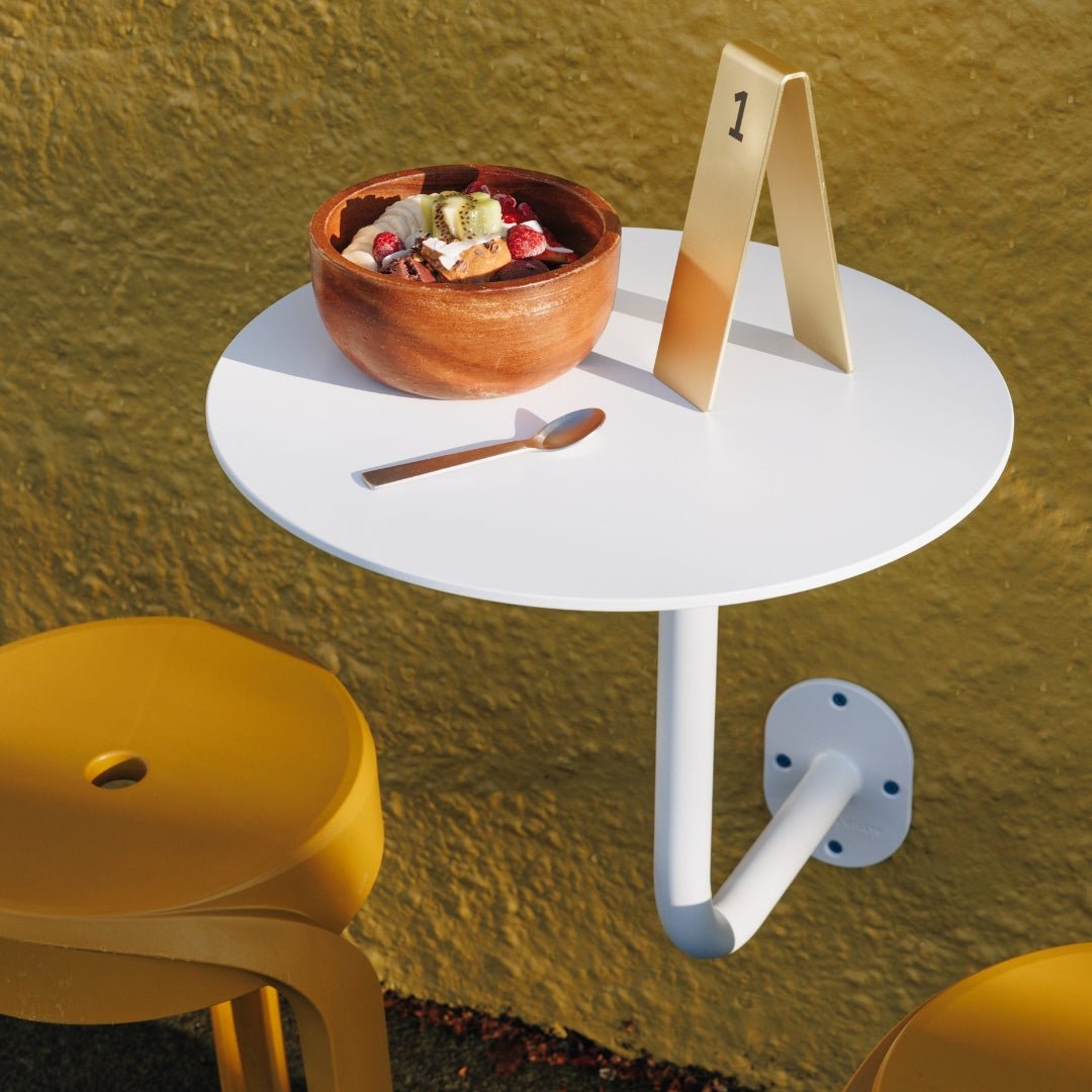 white wall mounted cafe table installed outside with table numbers on it