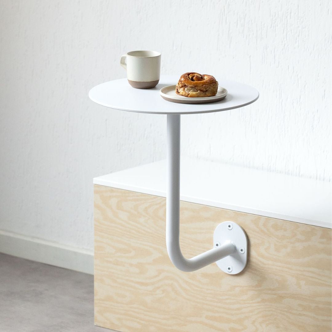 White wall-mounted table with coffee and pastry on top, showcasing a compact cafe table 