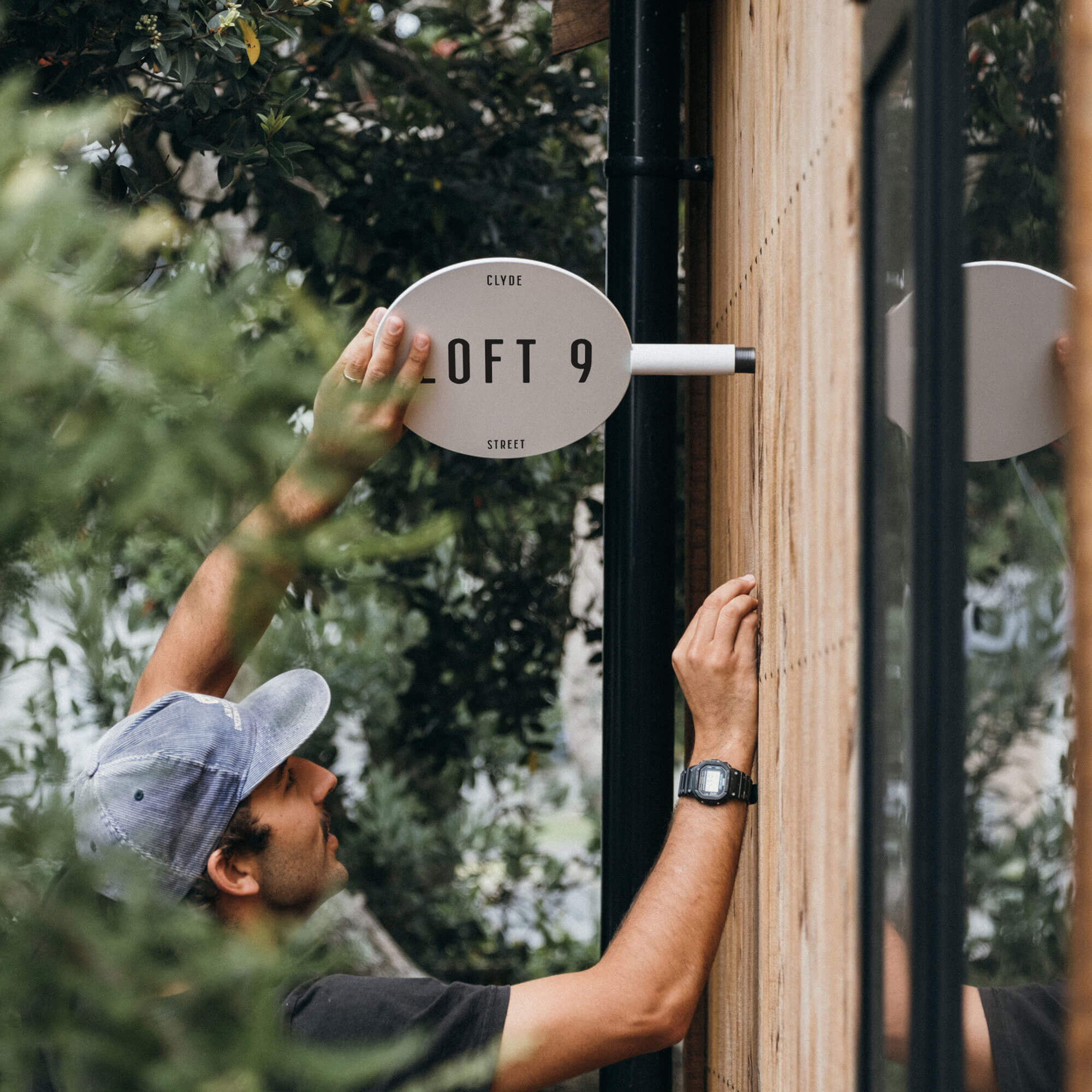 person installing white circle sign against a wooden wall outside a shopfront