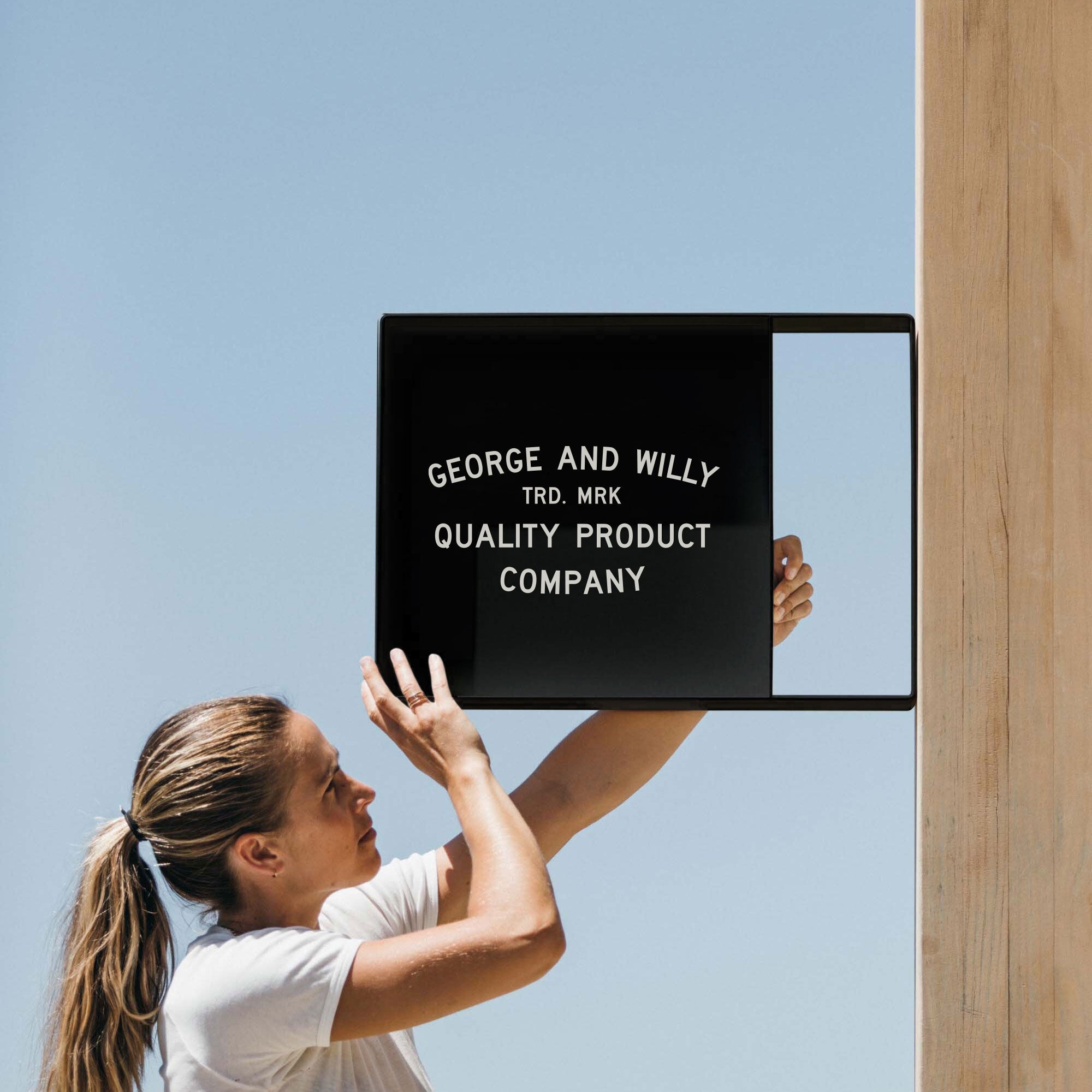 girl putting up the black square metal wall shopfront sign on a wooden beam