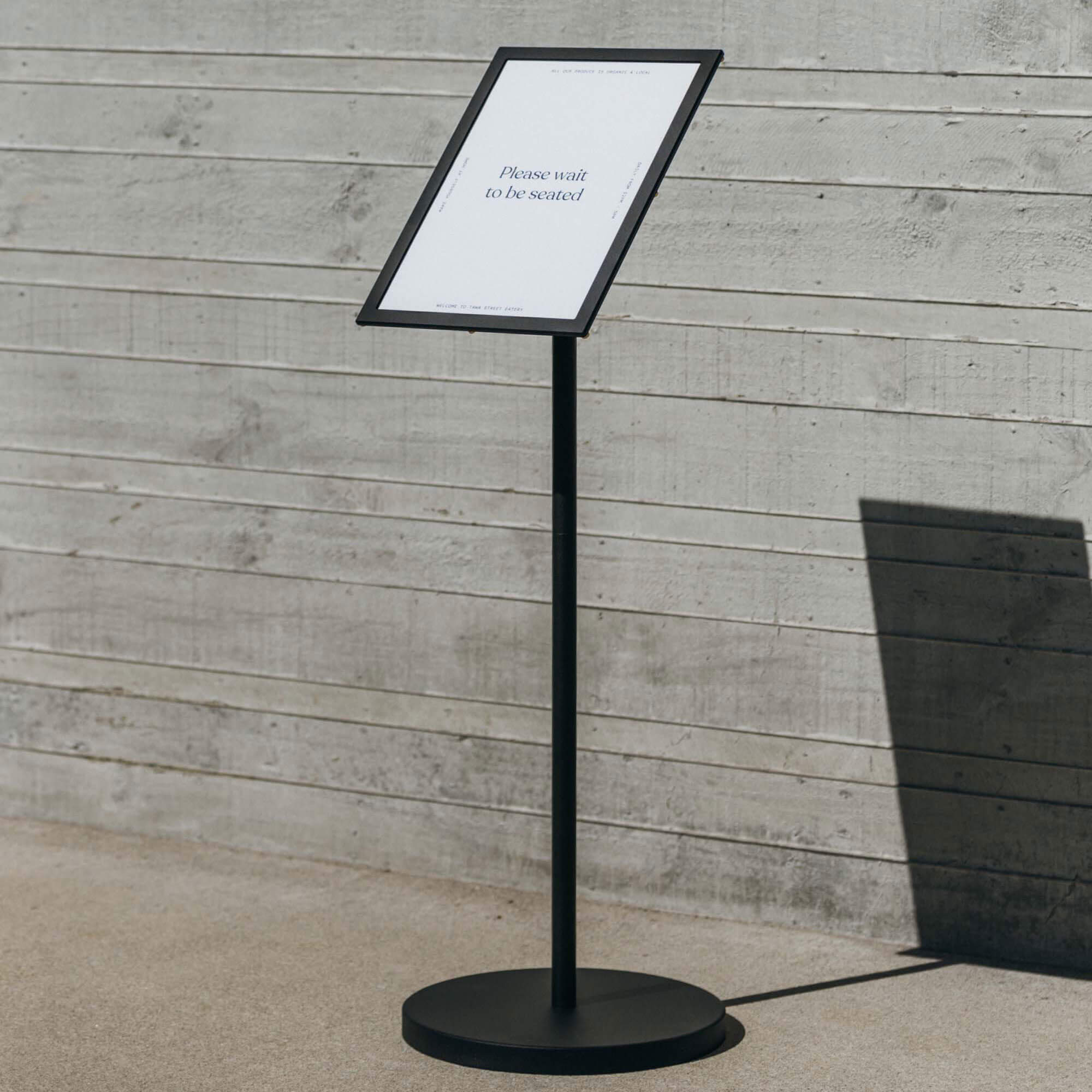 black menu stand with menu displayed vertically in front of a concrete wall