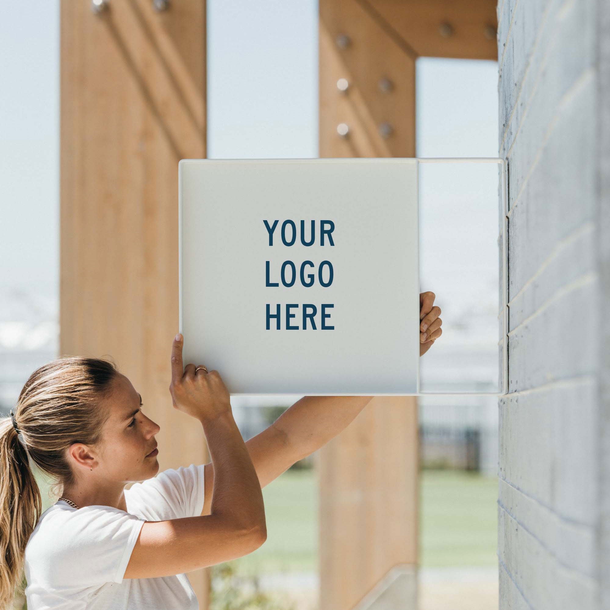 girl holding up white square panel wall sign on a cement wall
