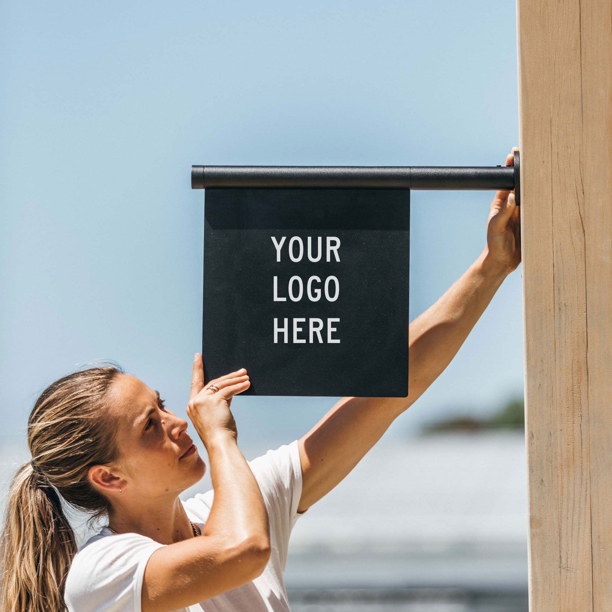 black wall hanging flag sign being installed by a girl on a wooden beam